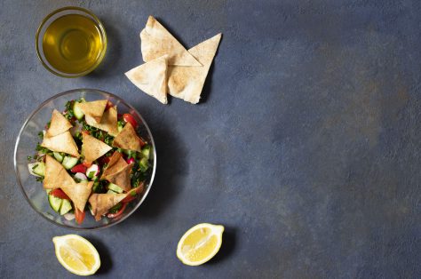 Traditional fattoush salad with vegetables pita bread levantine arabic middle eastern cuisine served glass plate with lemon pita olive oil dark background top view space text min