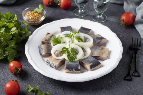 Salted herring slices with onion rings parsley white plate dark grey background